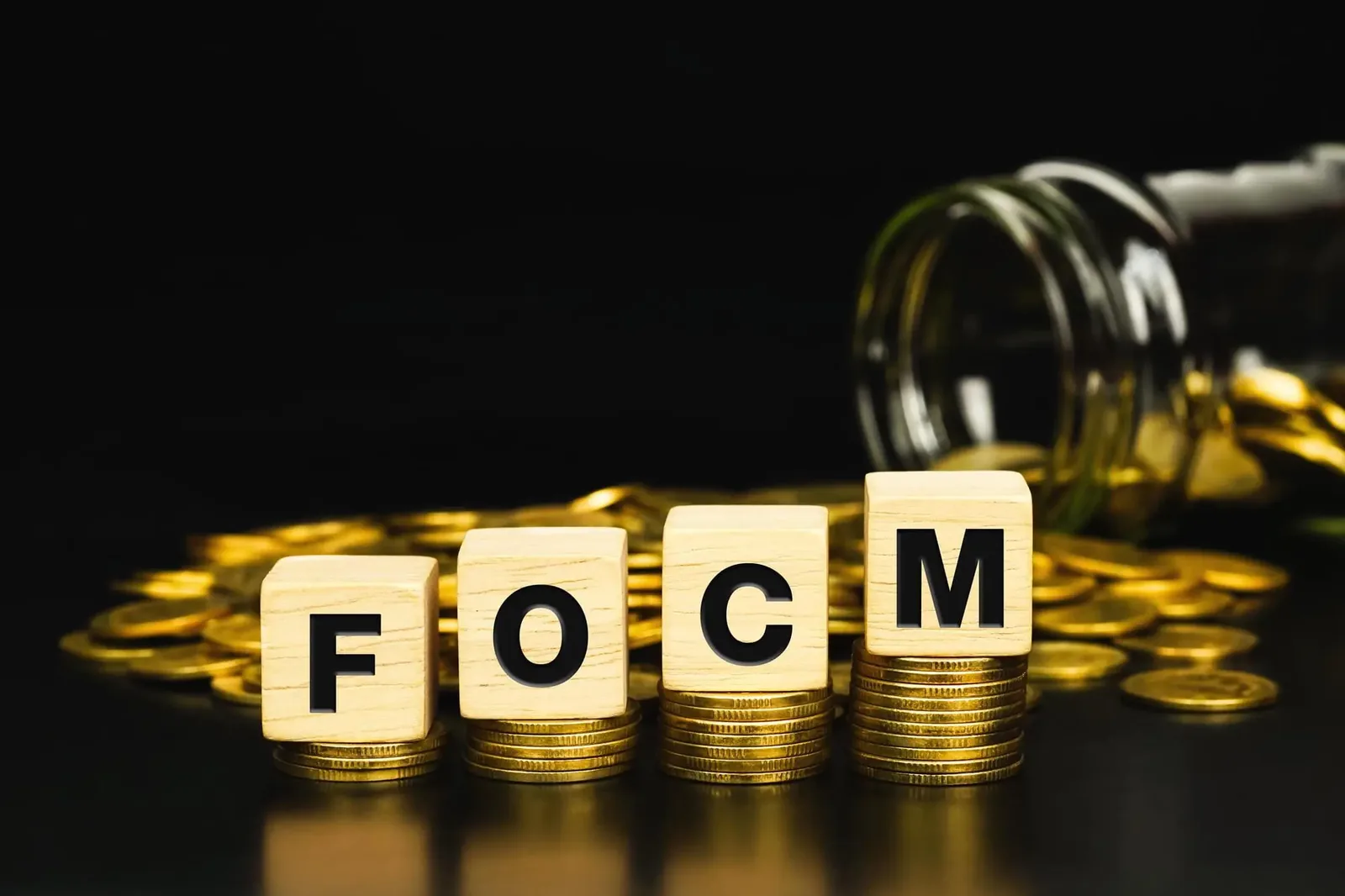 Text FOCM (Federal Open Market Committee) on wooden cube with stacks of gold coins. economic data
