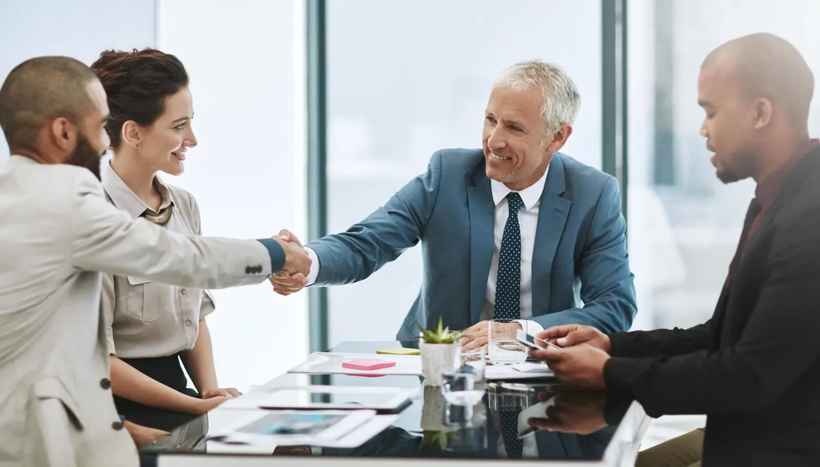 Business advisors shaking hands across a boardroom table during an M&A negotiation